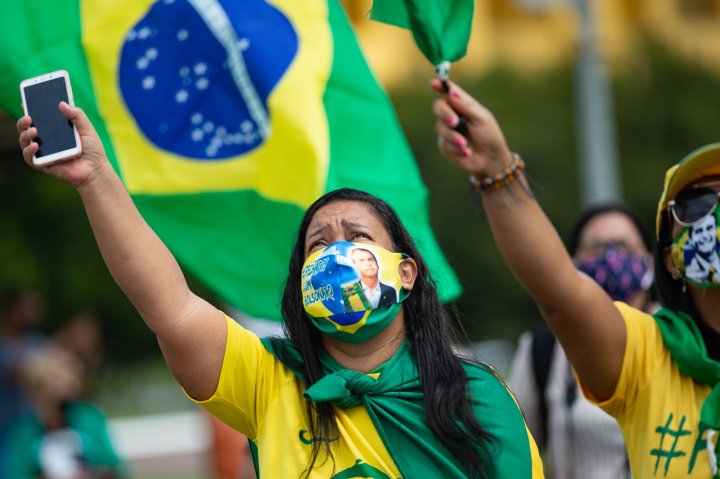 Supporters of Brazilian President Jair Bolsonaro wearing face masks with his face wave and shout slogans during a demonstration in favor of his government amidst the coronavirus pandemic in front of Planalto Palace on May 24, 2020 in Brasilia, Brazil. Brazil has over 352,000 confirmed positive cases of Coronavirus and 22,291 deaths. (Photo by Andressa Anholete/Getty Images)
