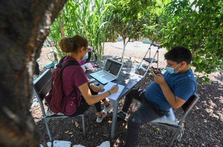 East College Prep High School senior Jocelyn Hernandez follows a remote Advanced Placement (AP) Calculus class as her cousin plays with his phone while sitting in a community garden near her home in the Boyle Heights neighborhood of Los Angeles, California. Due to the continuing coronavirus pandemic all Los Angeles Unified School District (LAUSD) schools will be closed and students will return to class via remote learning when the 2020-21 school year starts on August 18, 2020. (Photo by Robyn Beck / AFP)